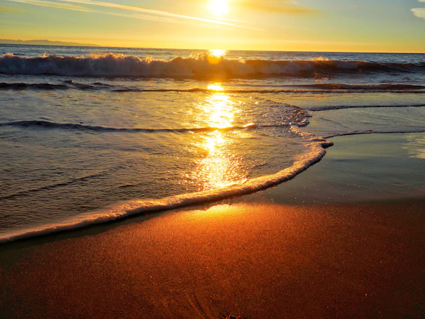 the sun is setting over the ocean on the beach