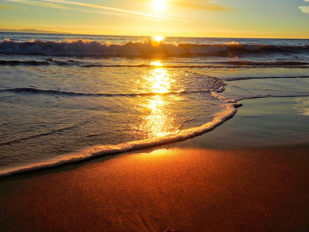 the sun is setting over the ocean on the beach