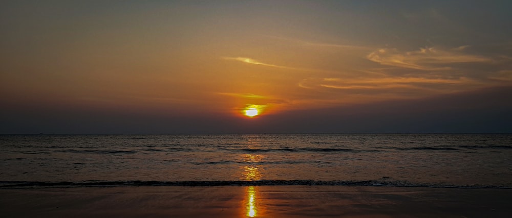 the sun is setting over the ocean on the beach