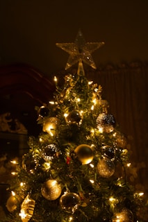 A lush, full artificial Christmas tree decorated with warm white lights and red ornaments in a cozy living room.