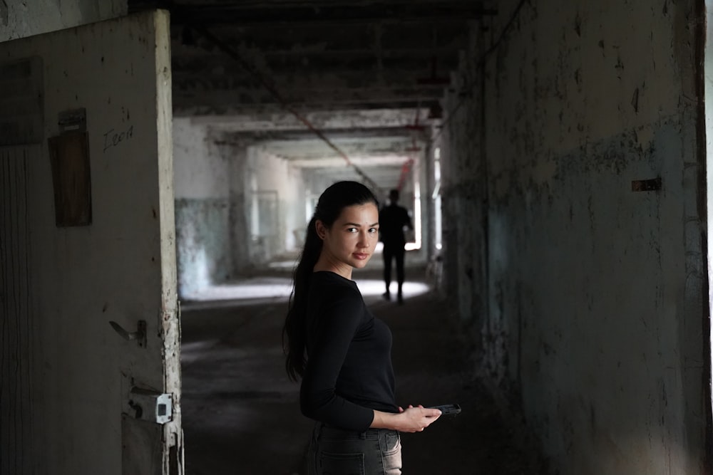 a woman standing in a dark hallway holding a remote control