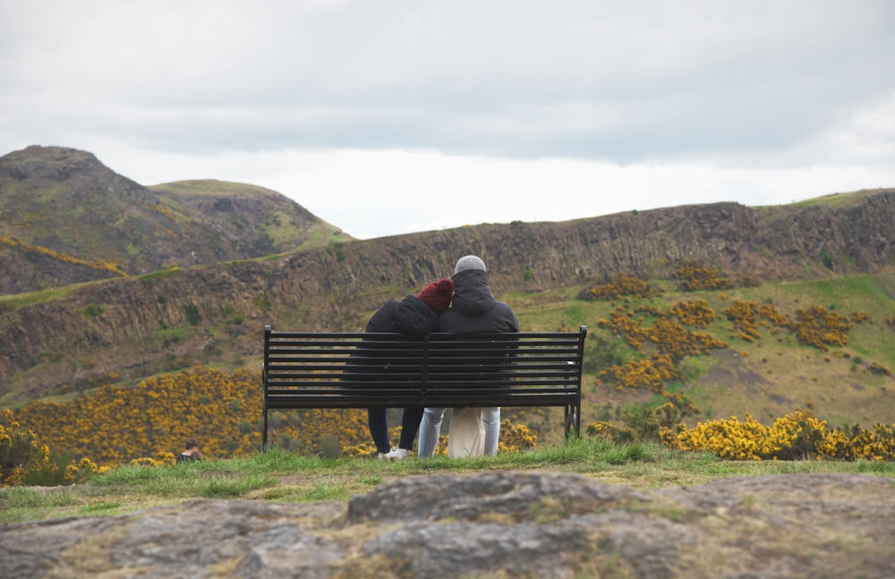 two people sitting on a bench in the mountains