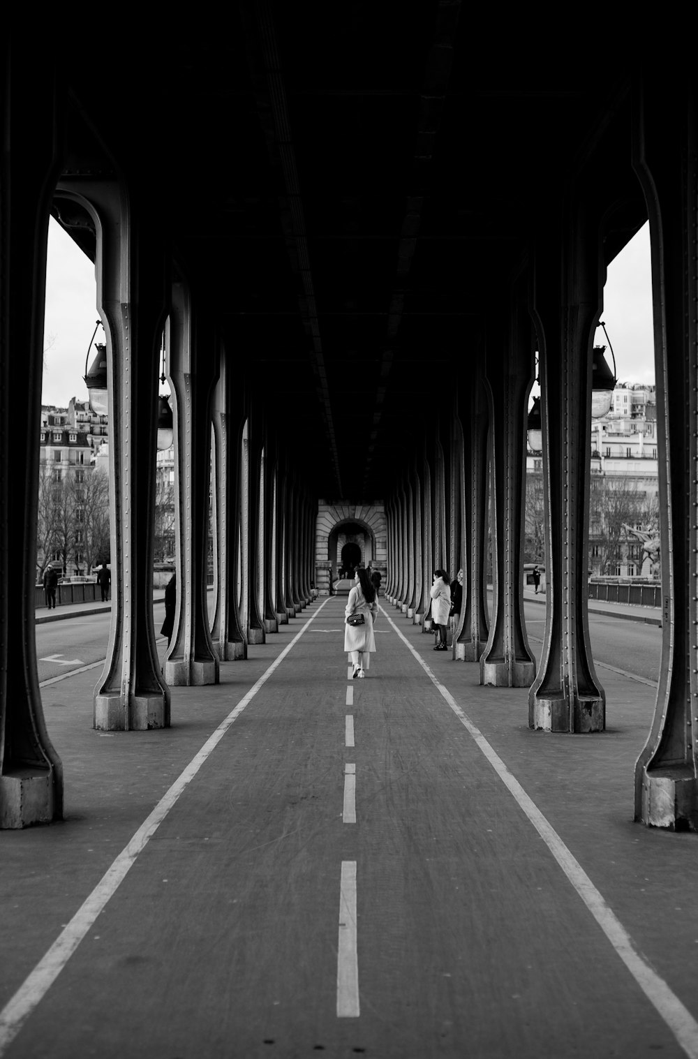 a black and white photo of a person walking under a bridge