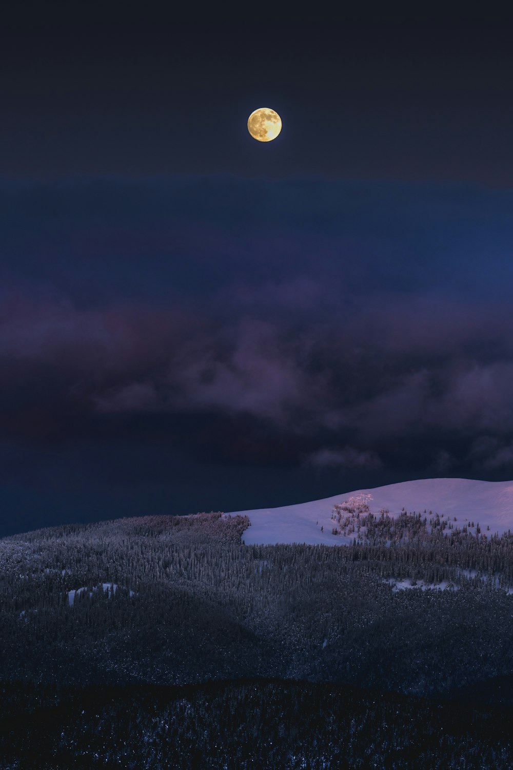 a full moon rising over a snowy mountain