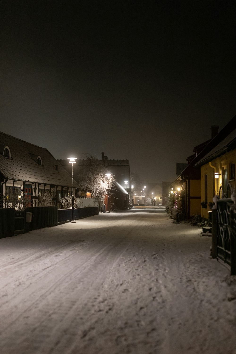 a snowy street at night with a bench in the foreground