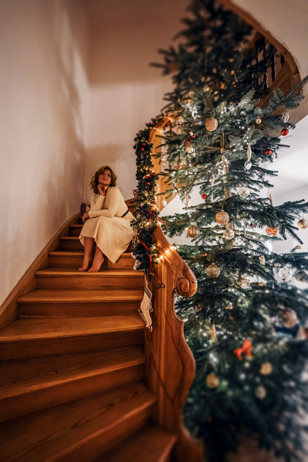 a woman sitting on the stairs next to a christmas tree