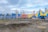A vibrant circus scene with a large striped yellow and blue tent. In front of the tent, several brightly colored trucks are parked, featuring bold and playful designs, alongside banners and fencing. Sparse trees and a cloudy sky form the backdrop.