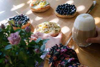 A colorful breakfast spread featuring a bagel with cream cheese, a breakfast burrito, and a cup of steaming coffee on a wooden table.