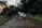 A white electric bike is parked on a muddy, forested trail. The path is surrounded by lush green vegetation and trees, with a peaceful, natural ambiance. The bike is positioned at an angle, highlighting its modern design and thick tires, suitable for off-road journeys.