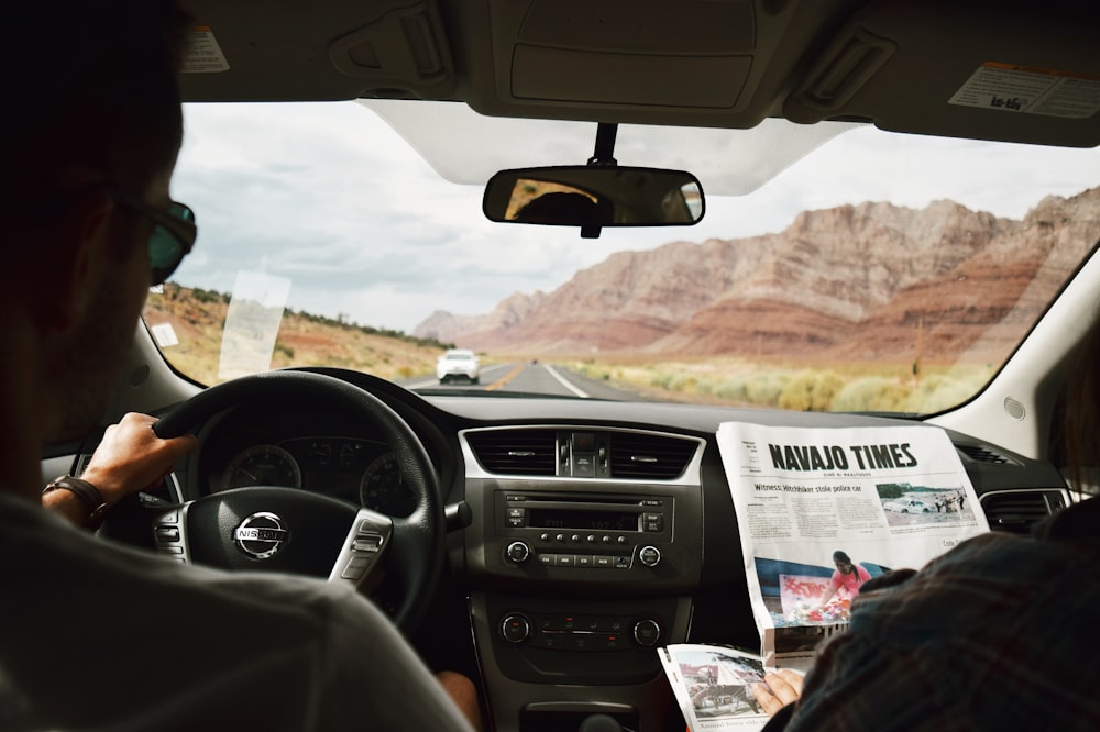 a man driving a car with a newspaper in his hand