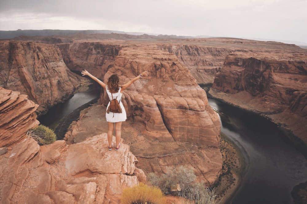 a woman standing on top of a cliff next to a river