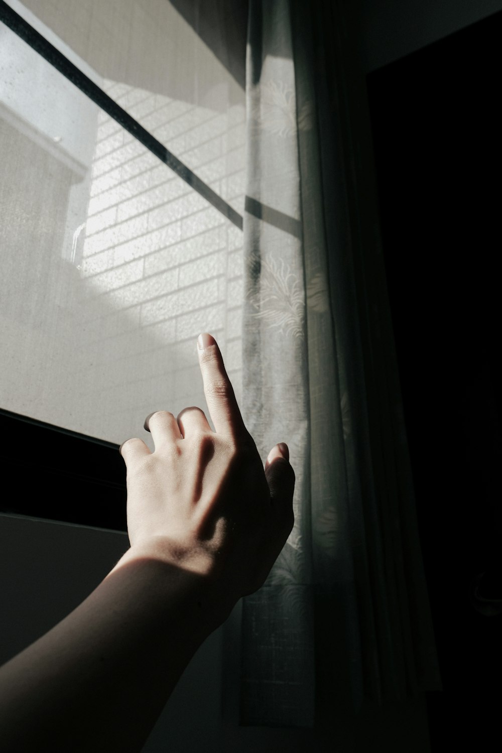 a person's hand pointing at a brick wall through a window