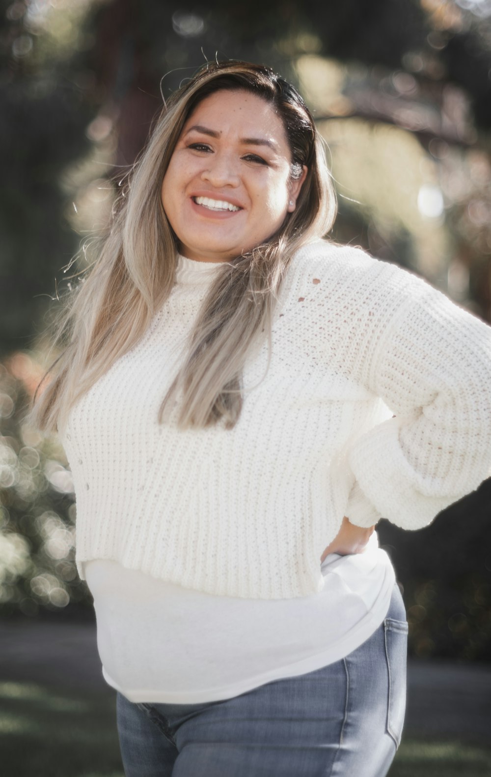 a smiling woman in a white sweater and jeans