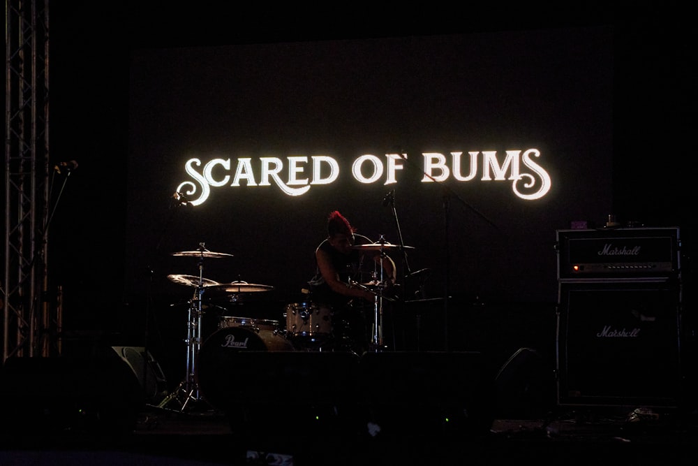 a man playing drums in front of a sign that reads scared of bums