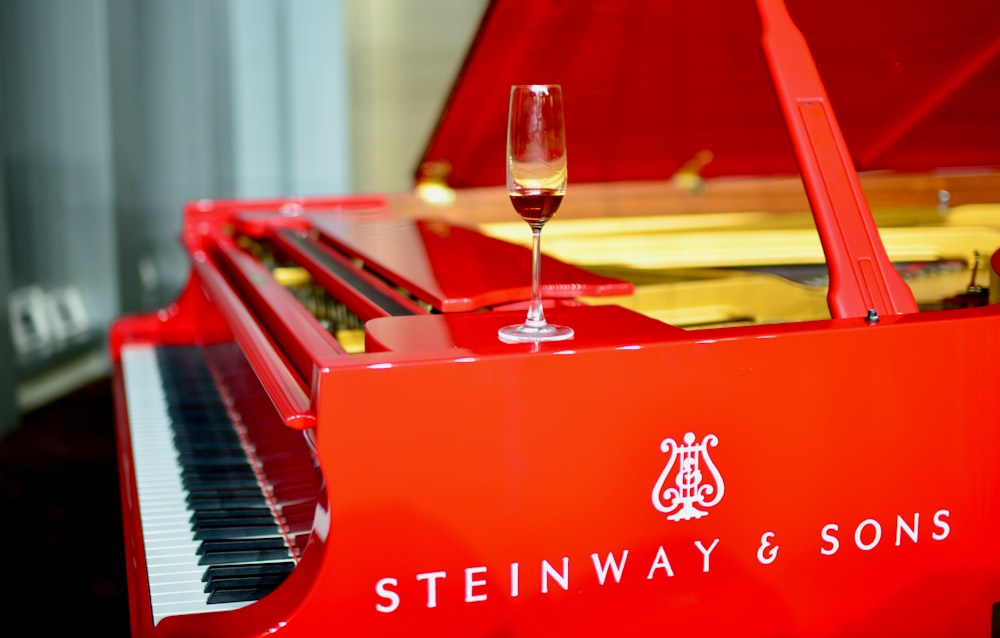 a glass of wine sitting on top of a red piano