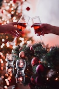 two people toasting with wine glasses in front of a christmas tree