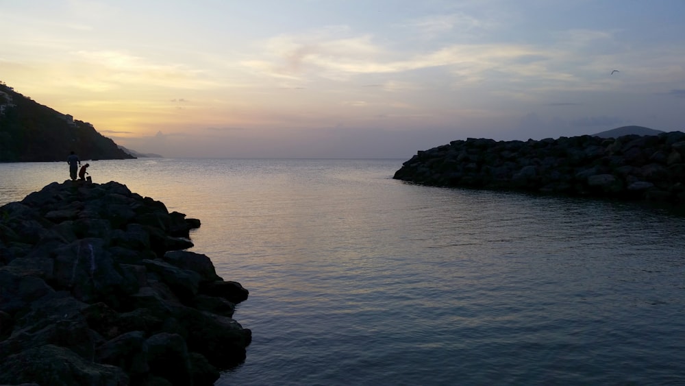 a couple of people standing on top of a rocky shore