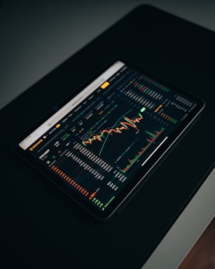 A tablet displaying a detailed digital financial trading interface with various graphs, charts, and numerical data. The screen shows candlestick charts with green and red indicators, illustrating market trends and stock prices.