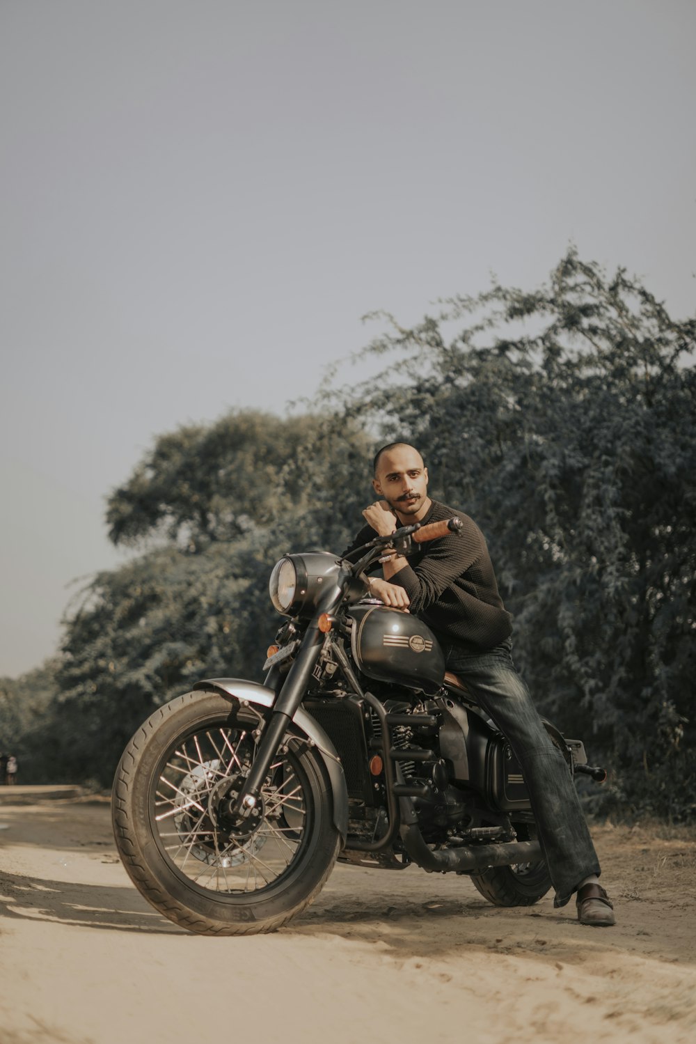 a man sitting on a motorcycle on a dirt road