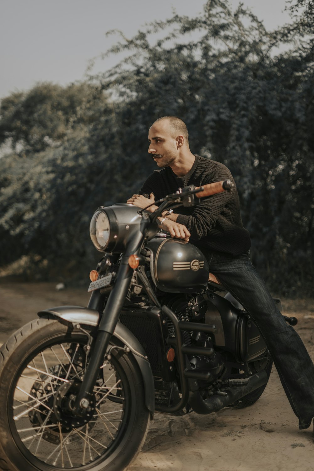 a man sitting on a motorcycle on a dirt road