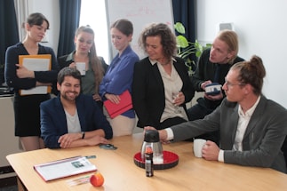 A professional office environment with people discussing over a table.