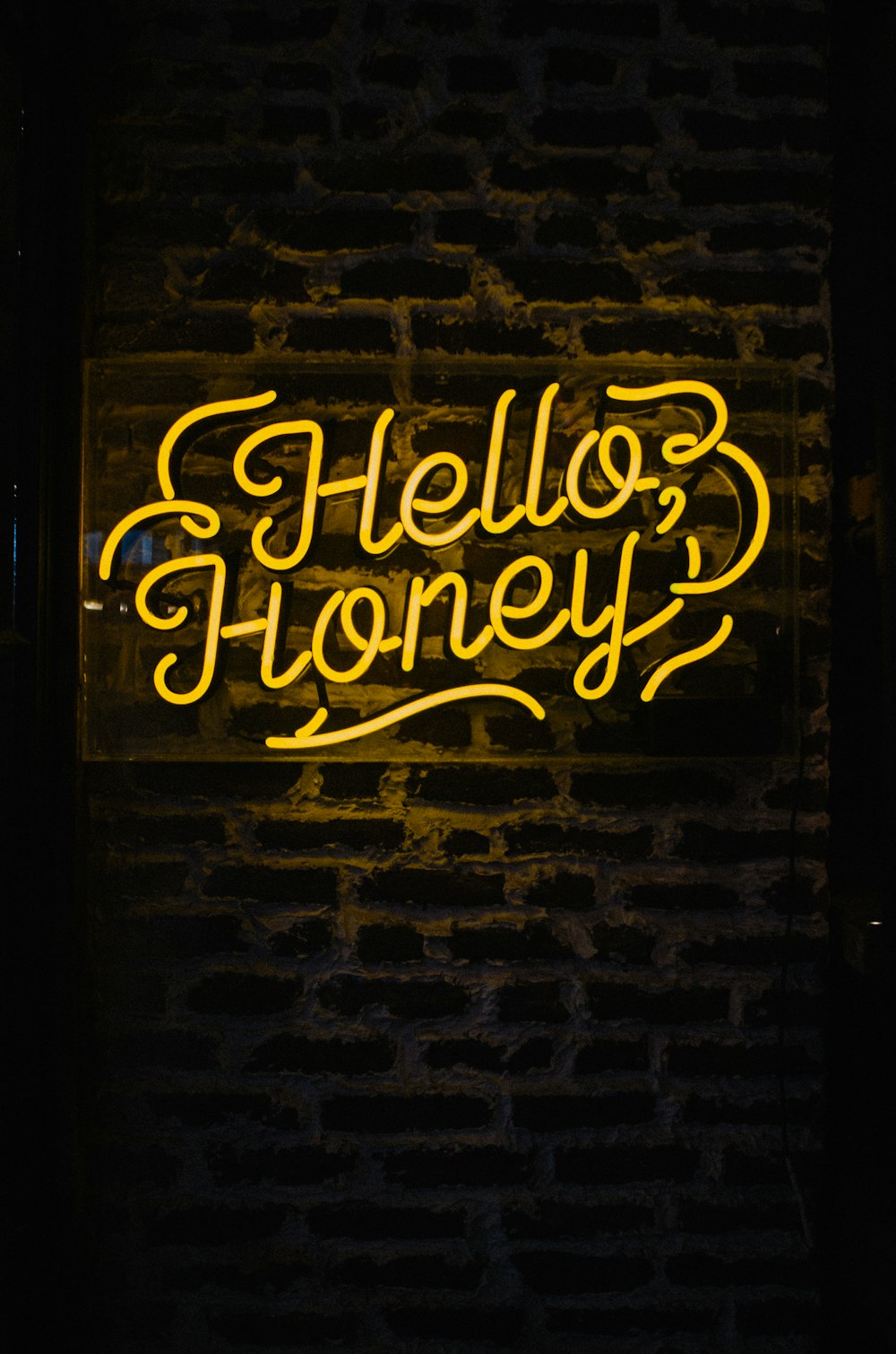 a neon sign that says hello honey on a brick wall