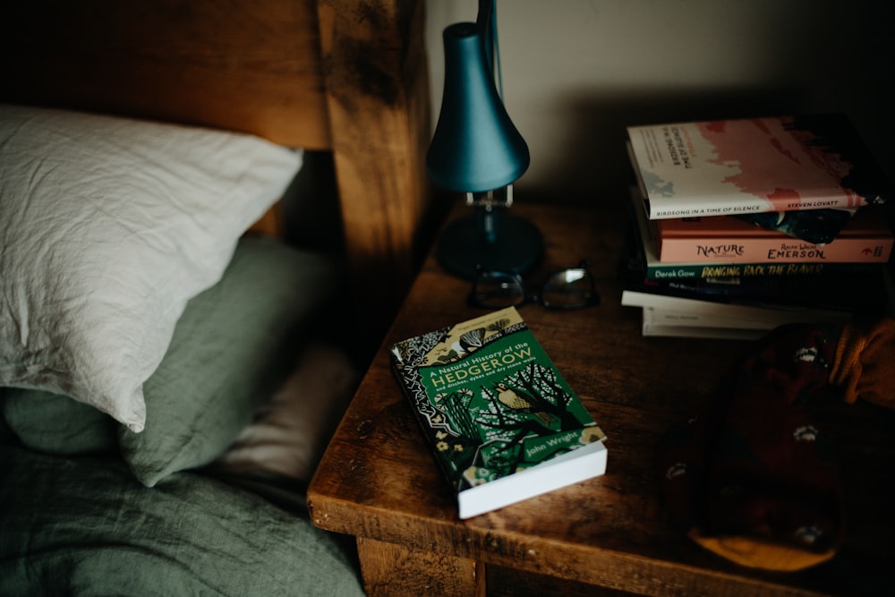 a stack of books sitting on top of a bed next to a lamp