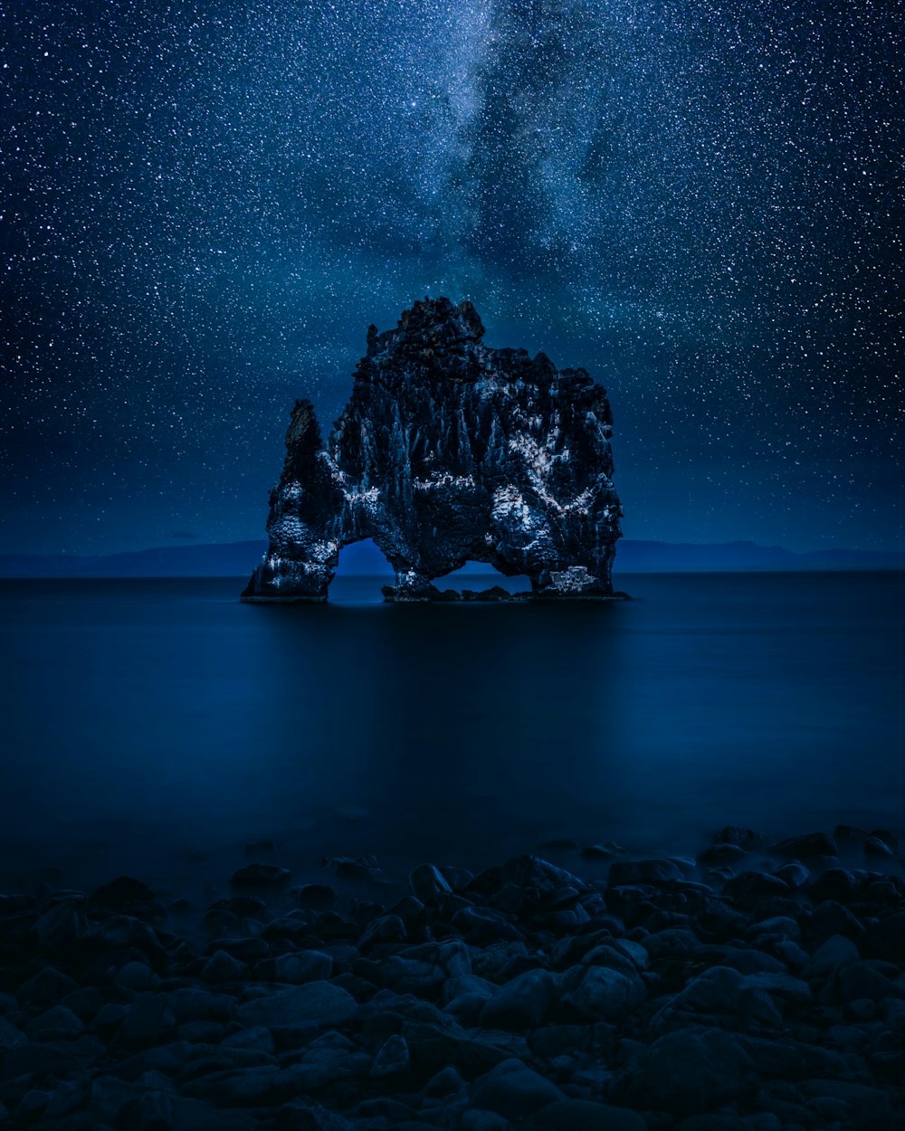 a rock formation in the middle of the ocean under a night sky filled with stars