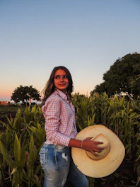 a woman standing in a field holding a hat