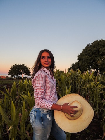 a woman standing in a field holding a hat