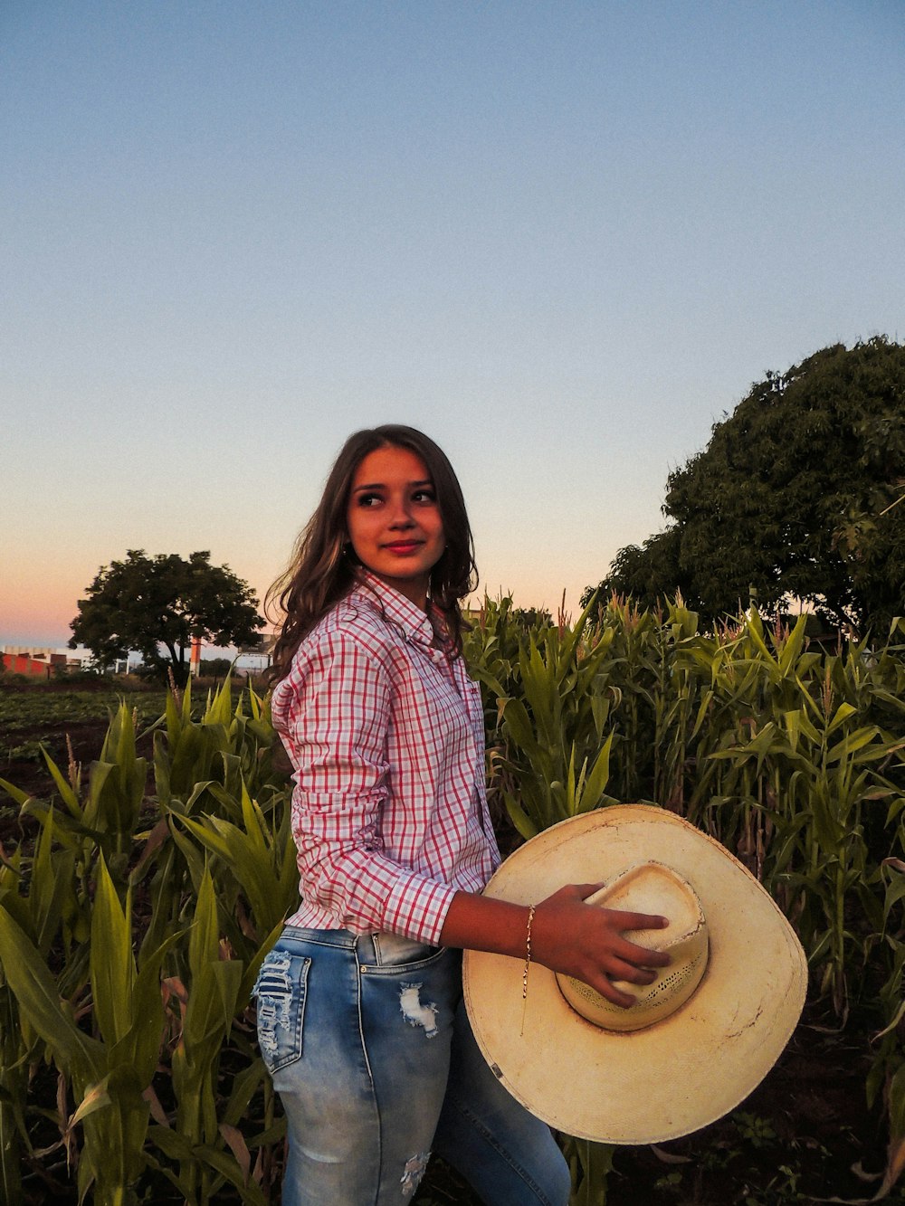 a woman standing in a field holding a hat