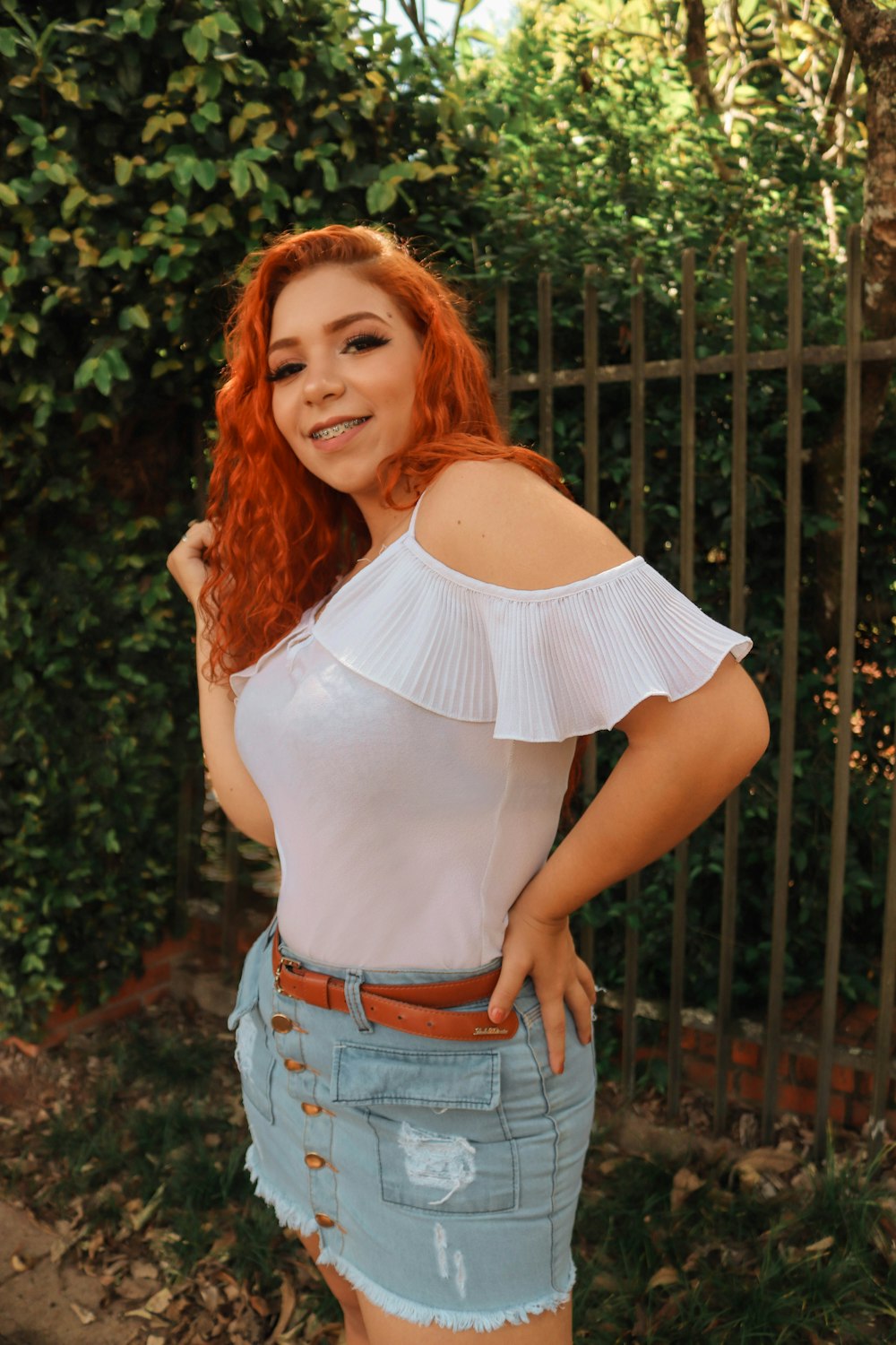 a woman with red hair wearing a white top and denim skirt