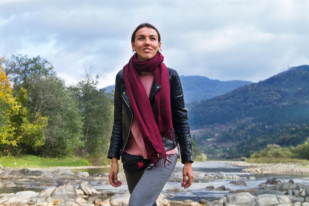a woman standing on a rocky river bank with a scarf around her neck