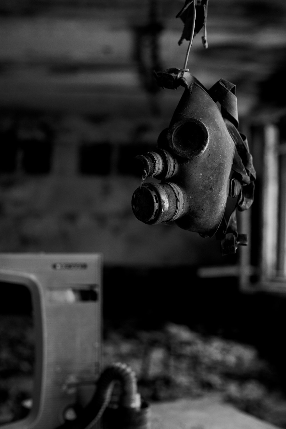 a black and white photo of a gas mask hanging from a hook