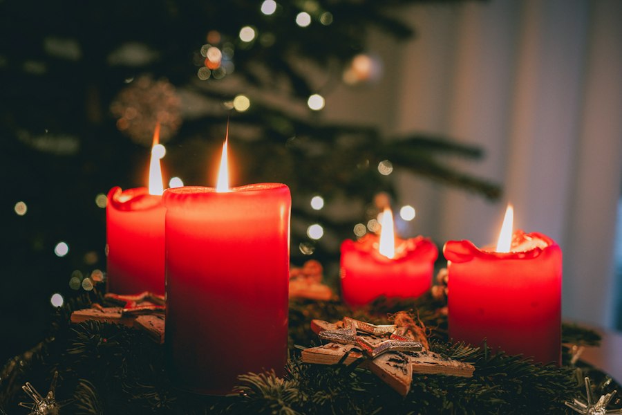 Four red candles lit in front of a Christmas tree