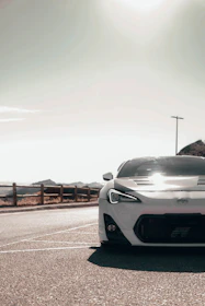 A stunning white sports car parked on a coastal road with mountains in the background.