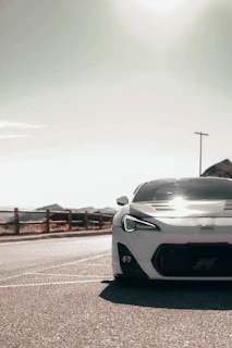 A stunning white sports car parked on a coastal road with mountains in the background.