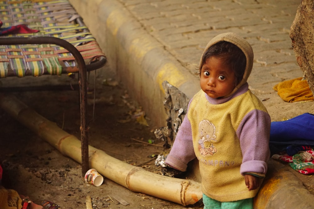 Un niño pequeño sentado en el suelo junto a una cama