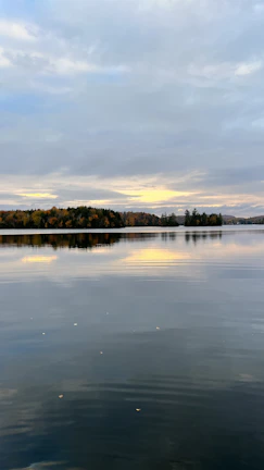 A serene lake reflecting autumn foliage under a soft sunset glow.