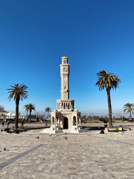 a clock tower in a plaza with palm trees