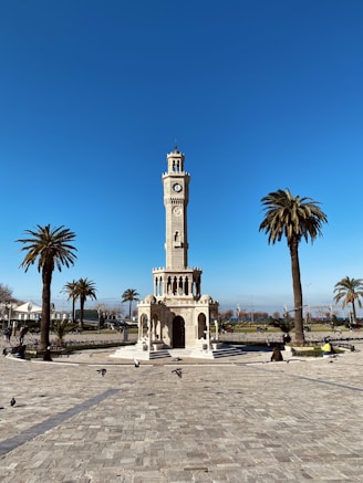 a clock tower in a plaza with palm trees
