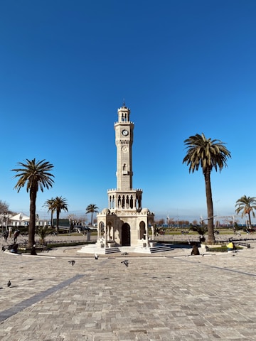 a clock tower in a plaza with palm trees
