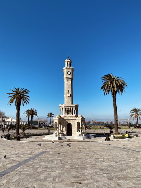 a clock tower in a plaza with palm trees