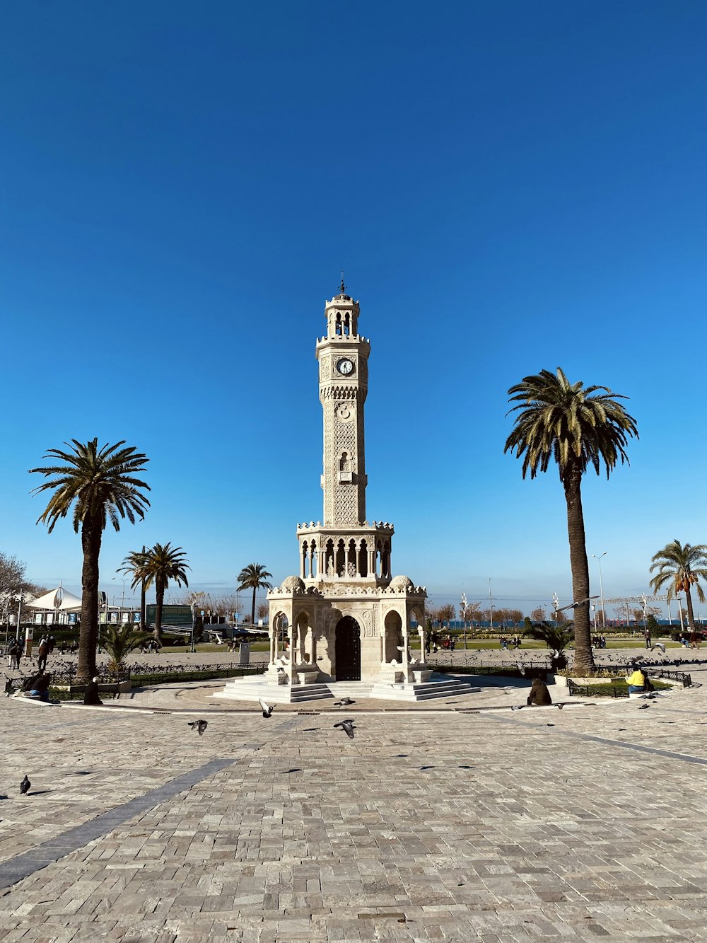 a clock tower in a plaza with palm trees