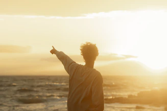 a man pointing at the sun over the ocean