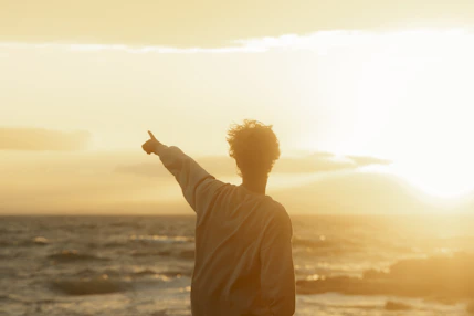 a man pointing at the sun over the ocean