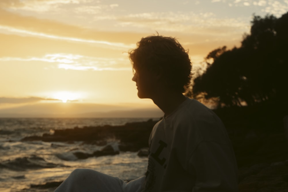 a man sitting on the beach watching the sunset