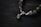 A close-up view of a bracelet featuring irregularly shaped metallic stones and a shiny metal clasp. The stones have a rough texture and give an earthy yet refined appearance. The background is a dark surface, emphasizing the subtle shine of the stones and clasp.