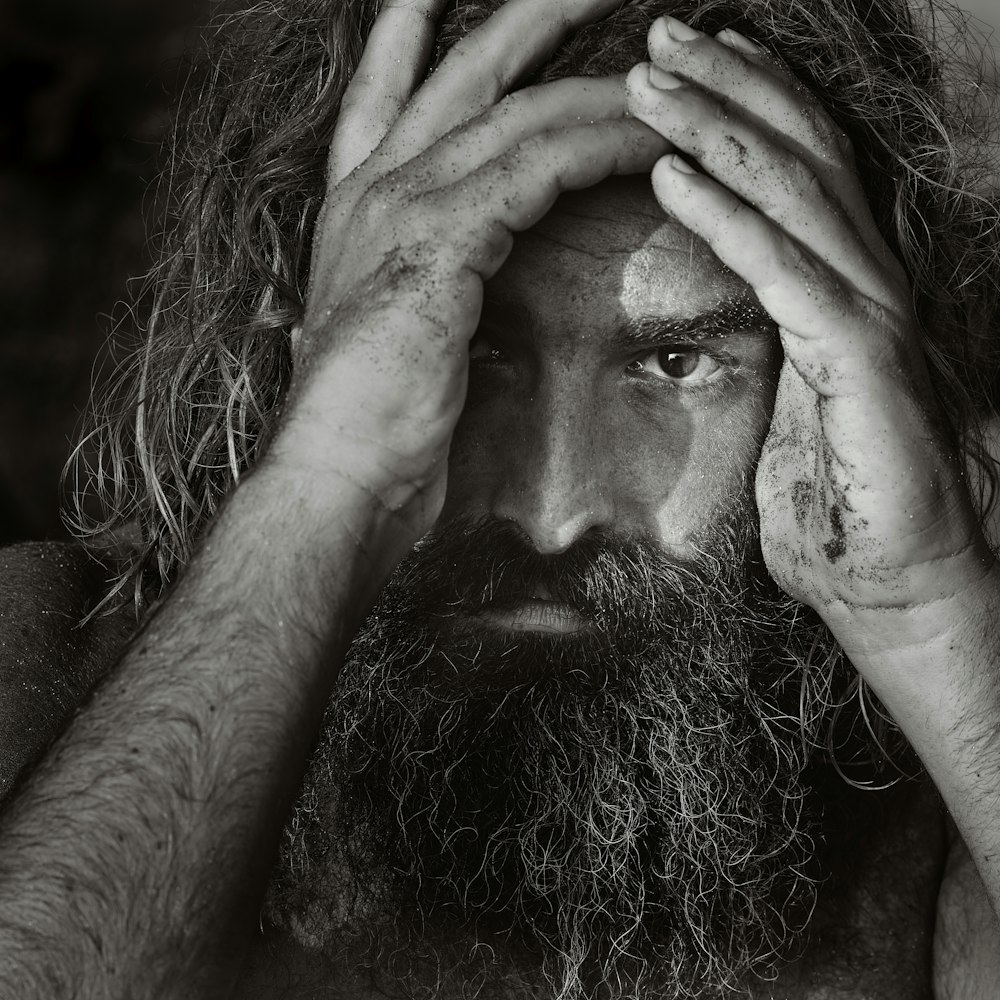 a man with long hair and a beard holding his hands to his face