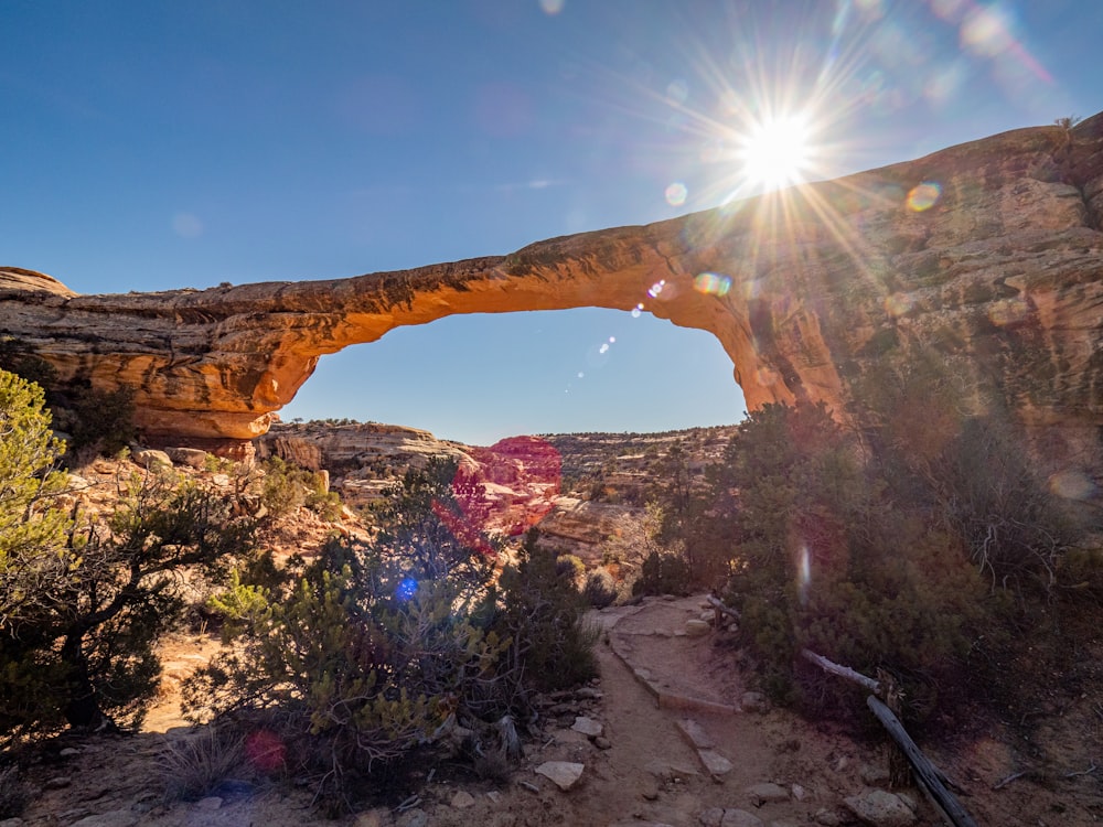 the sun shines brightly over a rock arch in the desert